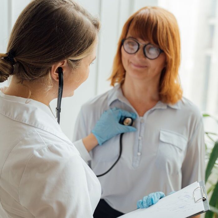 Home Doctor with stethoscope performing checkup on patient indoors.
